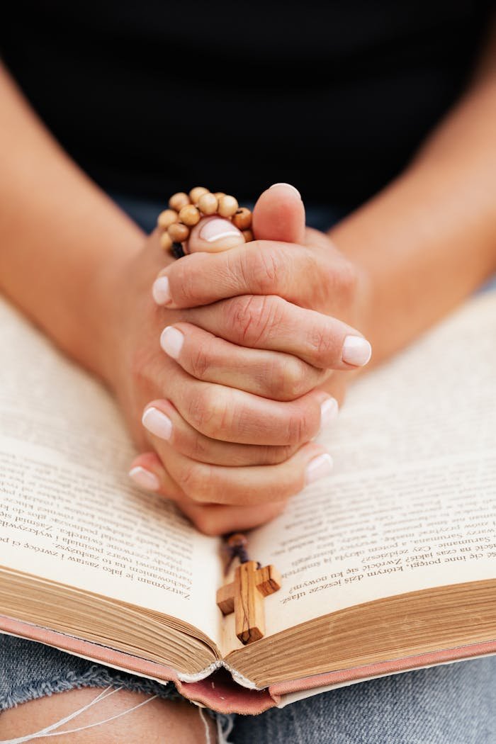 Close-up of hands holding a rosary while praying over an open Bible, symbolizing faith and devotion.